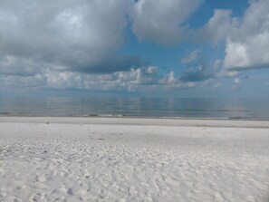 A beach with white sand and a calm sea under a partly cloudy sky.