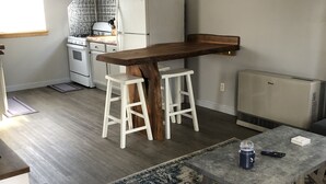 A compact kitchen with white appliances, a wooden bar counter, and a dining area with stools. - Sweet Escape Cottage on River  (Barton)