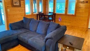 L'intérieur d'un chalet en bois comprend un grand canapé en forme de L, une table à manger avec des chaises et une petite table d'appoint.