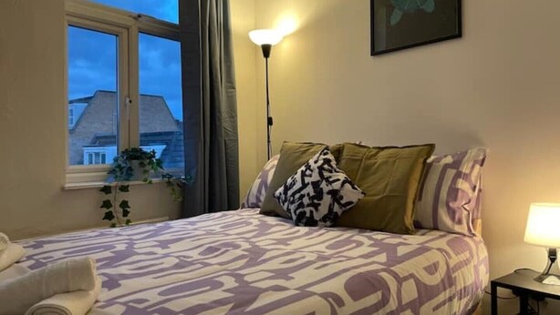Une chambre à coucher avec un lit, une fenêtre, une lampe et un tableau au mur.