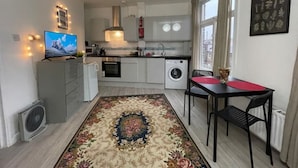 Un espace de vie compact comprenant une cuisine, un coin repas avec une table rouge et un grand tapis.