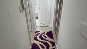 Un couloir étroit aux murs blancs et orné d’une moquette violette à motifs tourbillonnants blancs.
