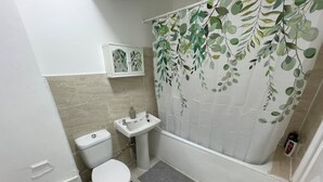 Une salle de bain équipée de toilettes, d’un lavabo et d’un rideau de douche orné d’un motif de feuilles.