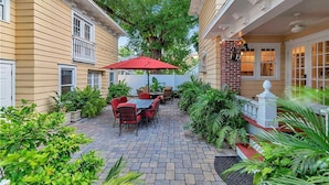 A patio with a table and chairs, surrounded by potted plants and a red umbrella. - Walnut Room at ONE Inn, Comfy, Steps to Downtown St. Pete: Ideal for all guests! (Saint Petersburg)