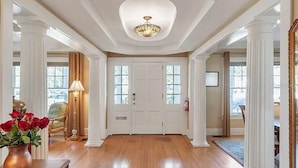 A spacious foyer with a wooden floor, white columns, a chandelier, and a door with windows. - Walnut Room at ONE Inn, Comfy, Steps to Downtown St. Pete: Ideal for all guests! (Saint Petersburg)