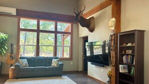 A living room with a large window, a mounted deer head, a TV, a bookshelf, and a guitar. - Abundant Activities for Adventurous People (Goldendale)