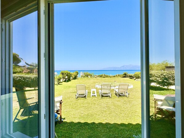 A view from a room with large windows overlooking a grassy area with several lounge chairs and a table.