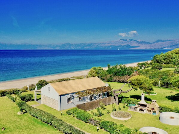 A coastal property with a house, a barbecue area, and a view of the sea and mountains.