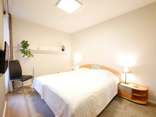 A bedroom with a bed, bedside tables, a chair, a TV, a radiator, and a plant. - Erdgeschosswohnung mit Eigenem Parkplatz Vorm Haus in Ruhiger Zentraler Lage (Osnabrück)