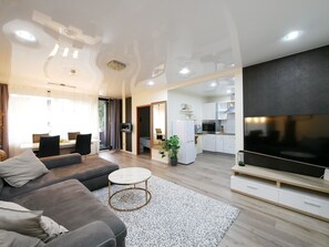 A modern living room with a grey sofa, a round coffee table, and a TV. There is a kitchen area with white cabinets and a black countertop. - Erdgeschosswohnung mit Eigenem Parkplatz Vorm Haus in Ruhiger Zentraler Lage (Osnabrück)