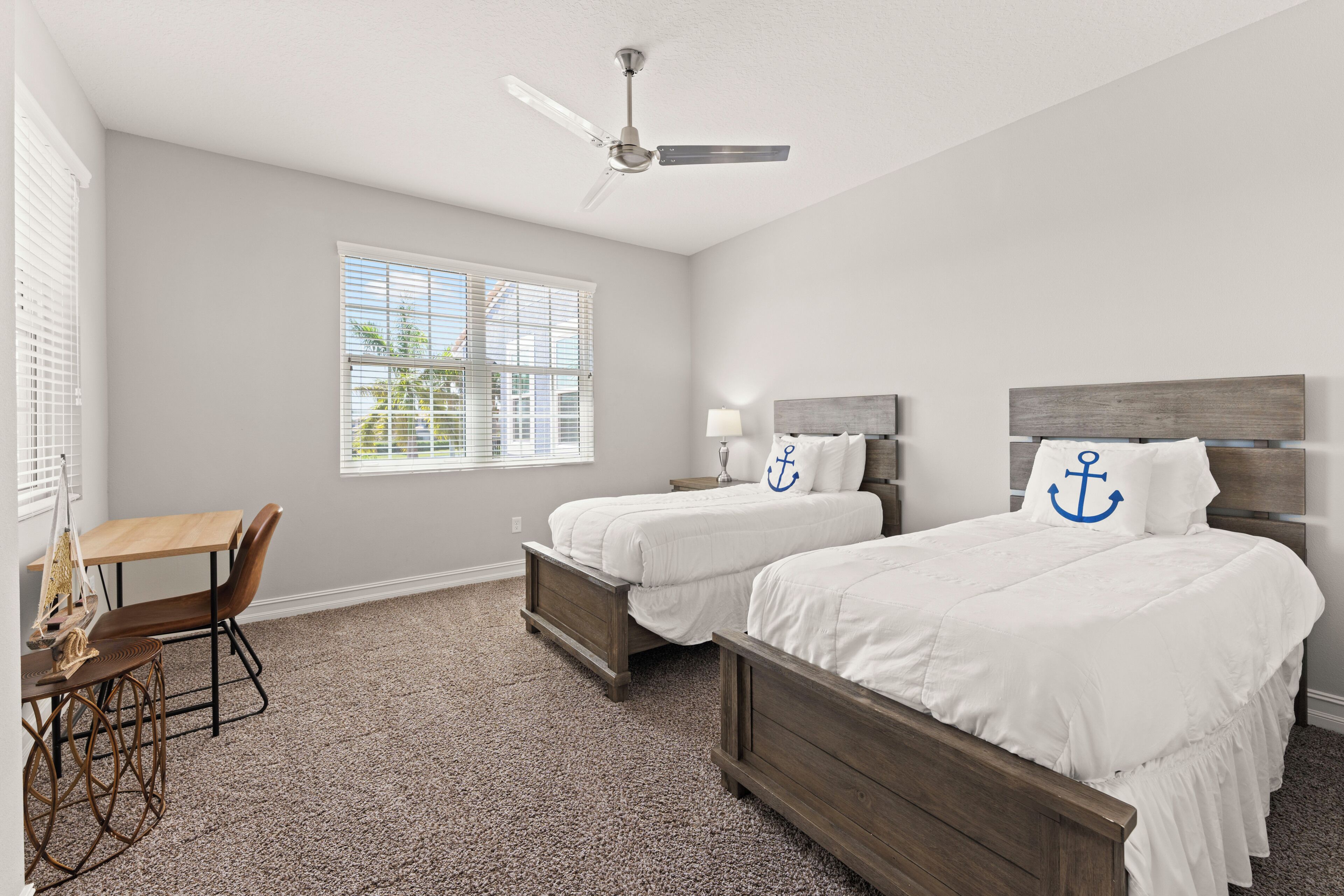 A bedroom with two beds, a desk, and a ceiling fan.