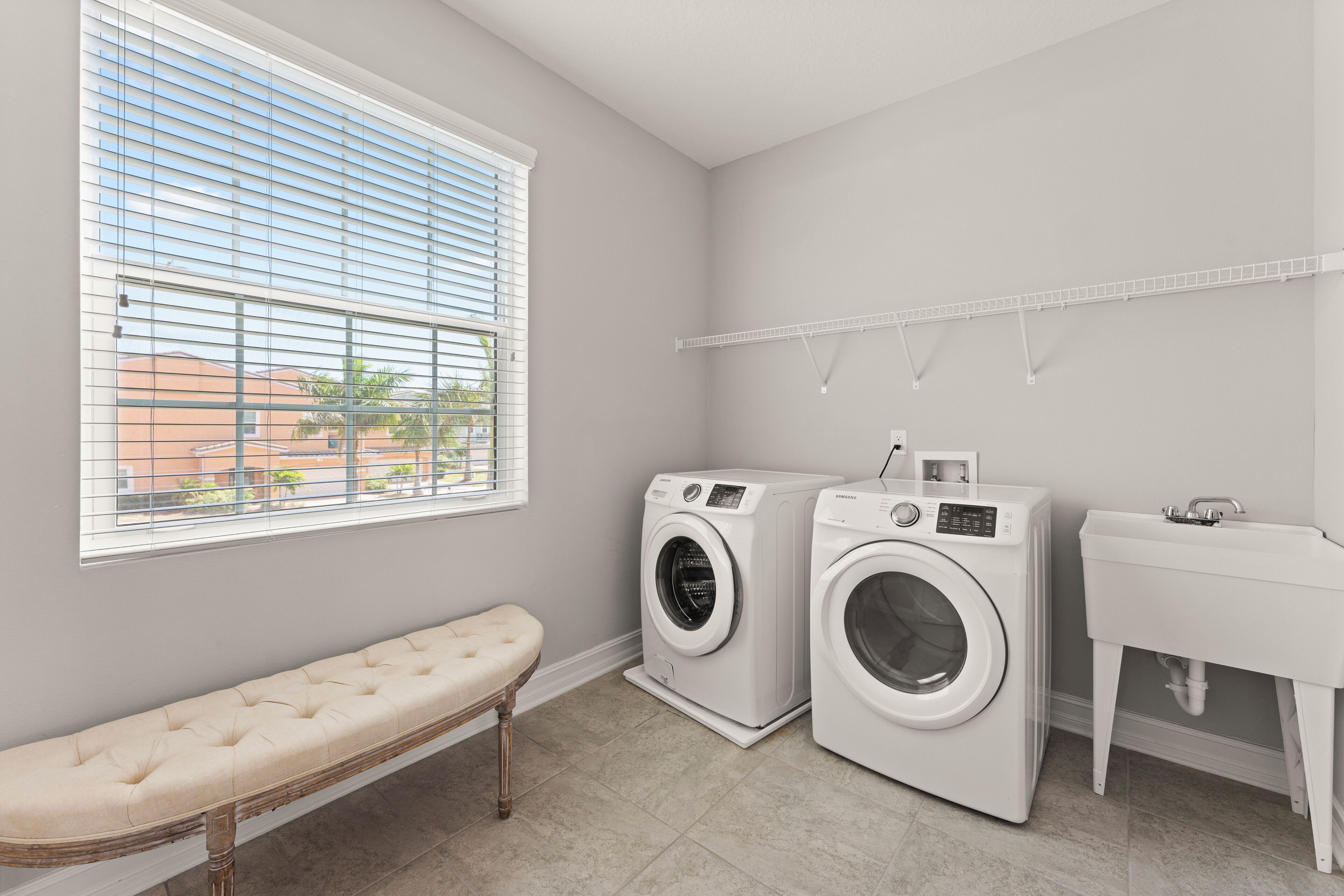 A laundry room with two washing machines, a bench, a sink, and a window with blinds.