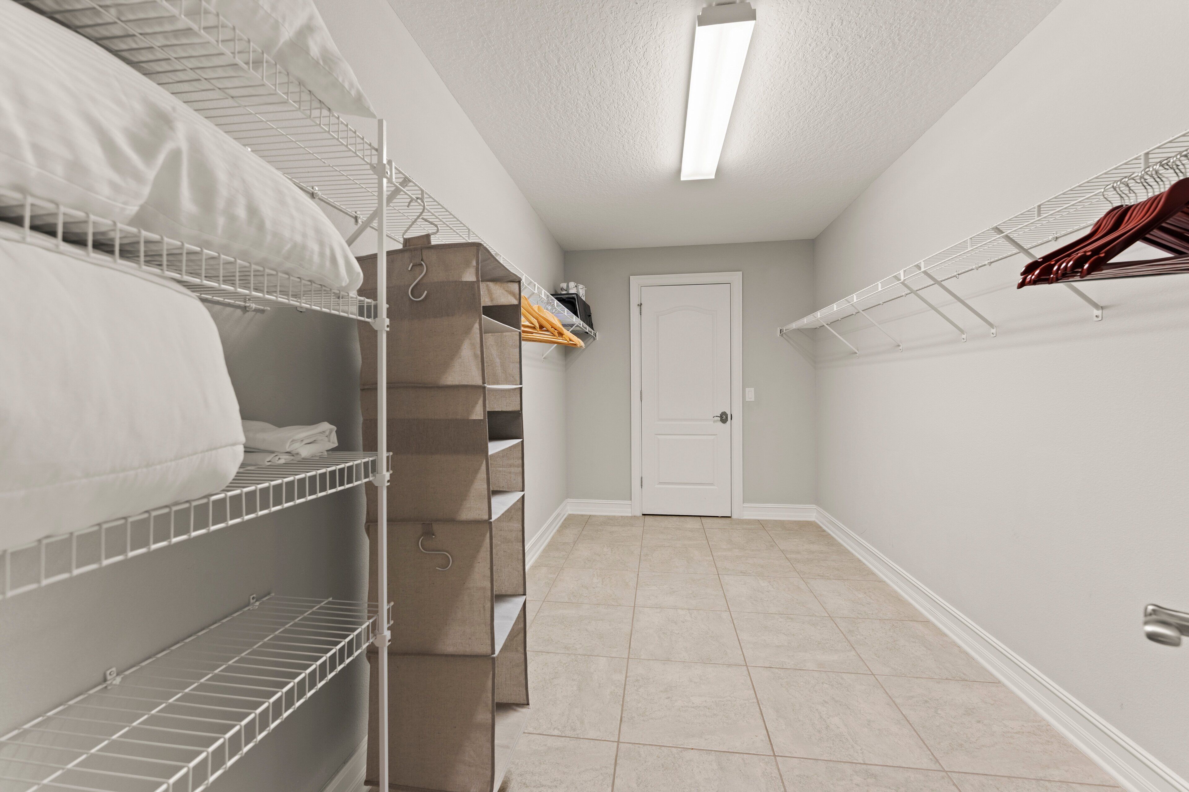 Um closet amplo com prateleiras de metal, porta branca e chão revestido com azulejos.