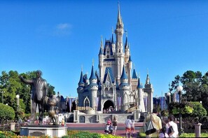 A castle-like structure with multiple towers and a central entrance, surrounded by greenery and a statue.