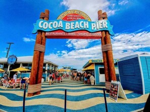 The entrance to Cocoa Beach Pier with a sign indicating it offers restaurants, bars, shops, and fishing. - 200 Madison Avenue (Cape Canaveral)