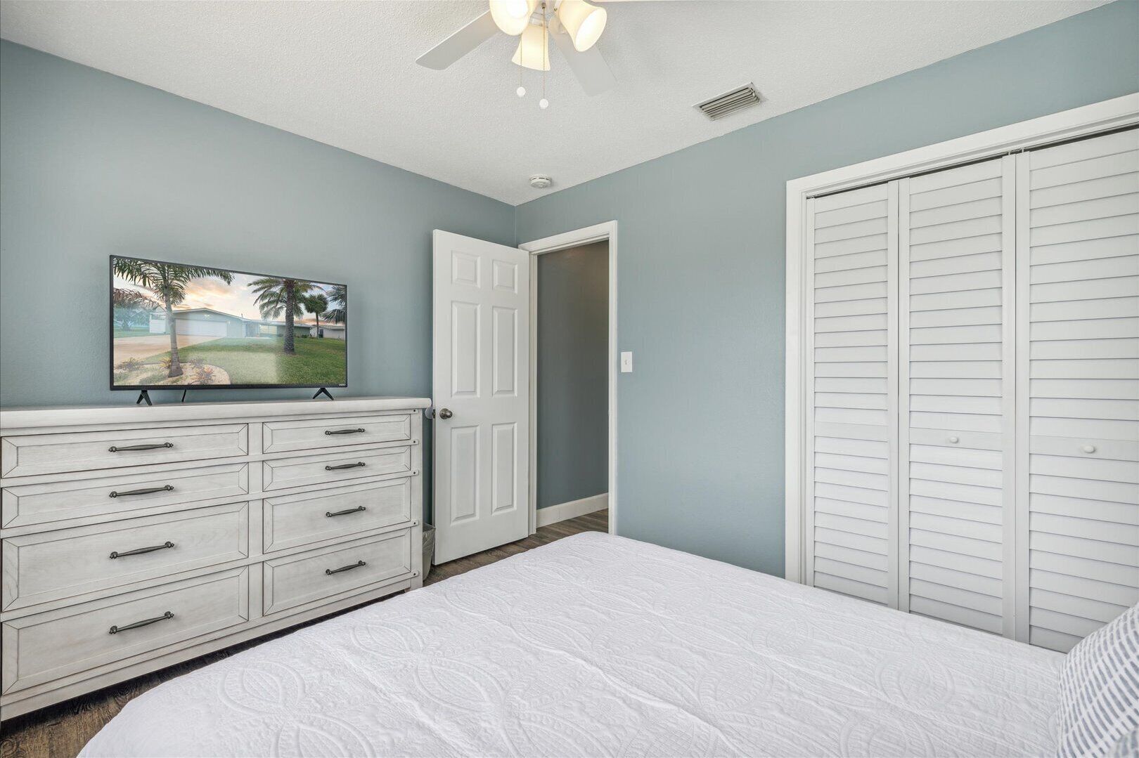 A bedroom with a bed, a dresser, a television, and a closet.