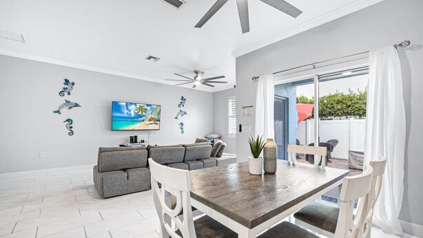 A modern living room with a grey sofa, a wooden dining table, and a ceiling fan. - 8023 Magnolia Ave (Cape Canaveral)