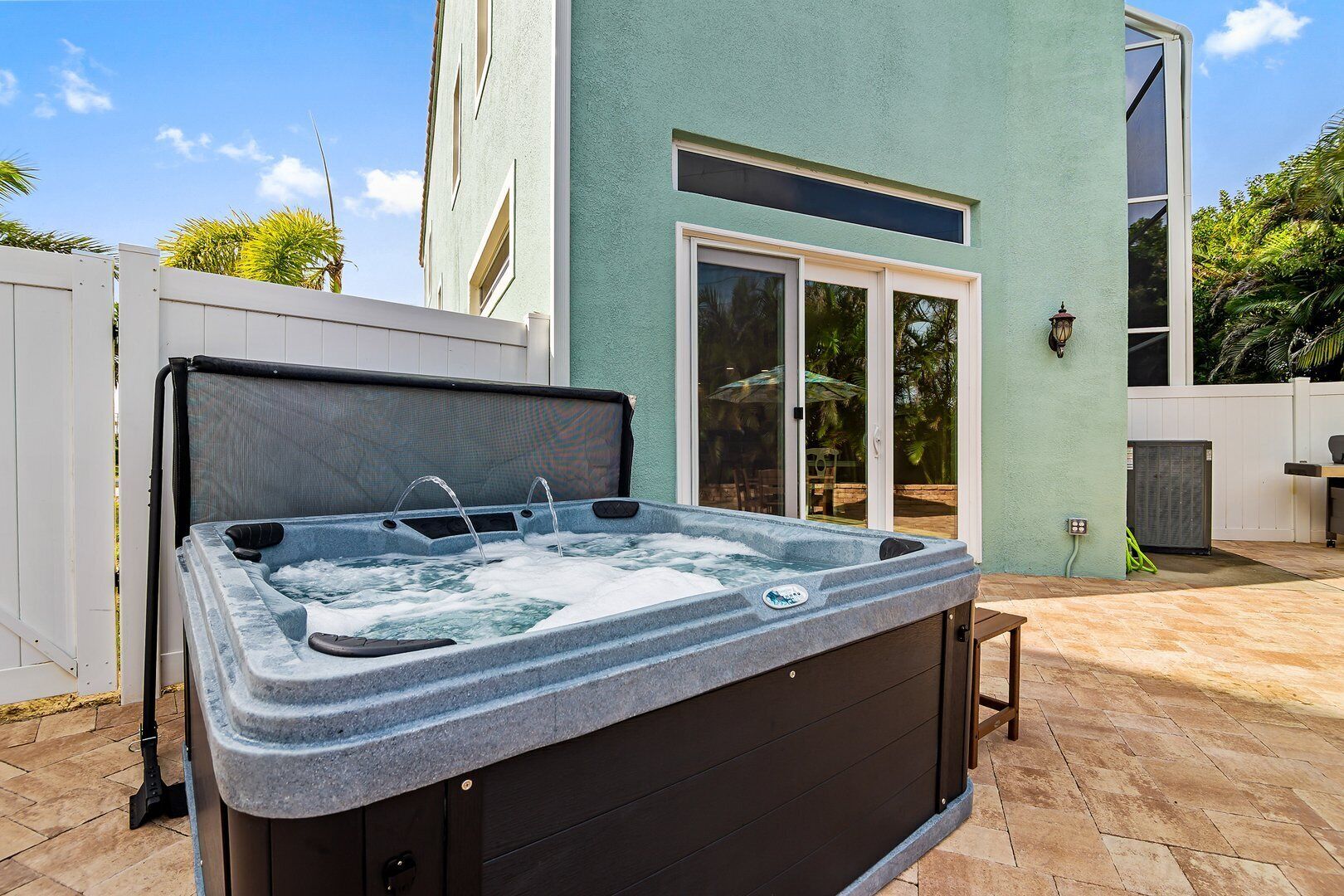 A hot tub in an outdoor patio area with a sliding glass door leading to a covered outdoor space.