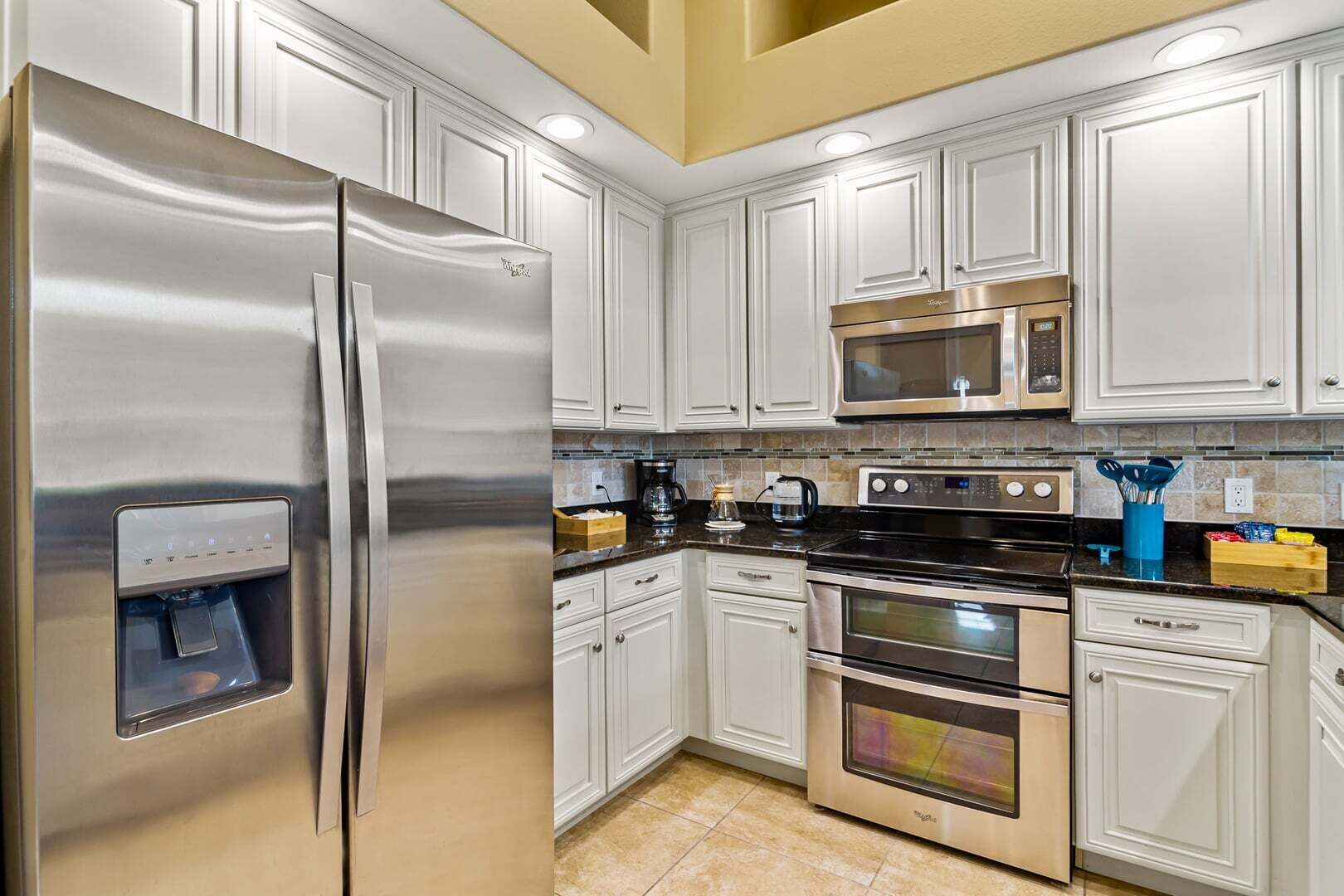 A modern kitchen with stainless steel appliances, white cabinetry, and a built-in water dispenser.