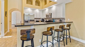 Een ruime keuken met witte kastjes, een centraal kookeiland met barstoelen, en een moderne, roestvrijstalen koelkast.