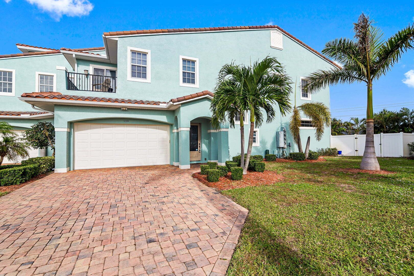 A two-story house with a garage, a brick driveway, and palm trees in the yard.