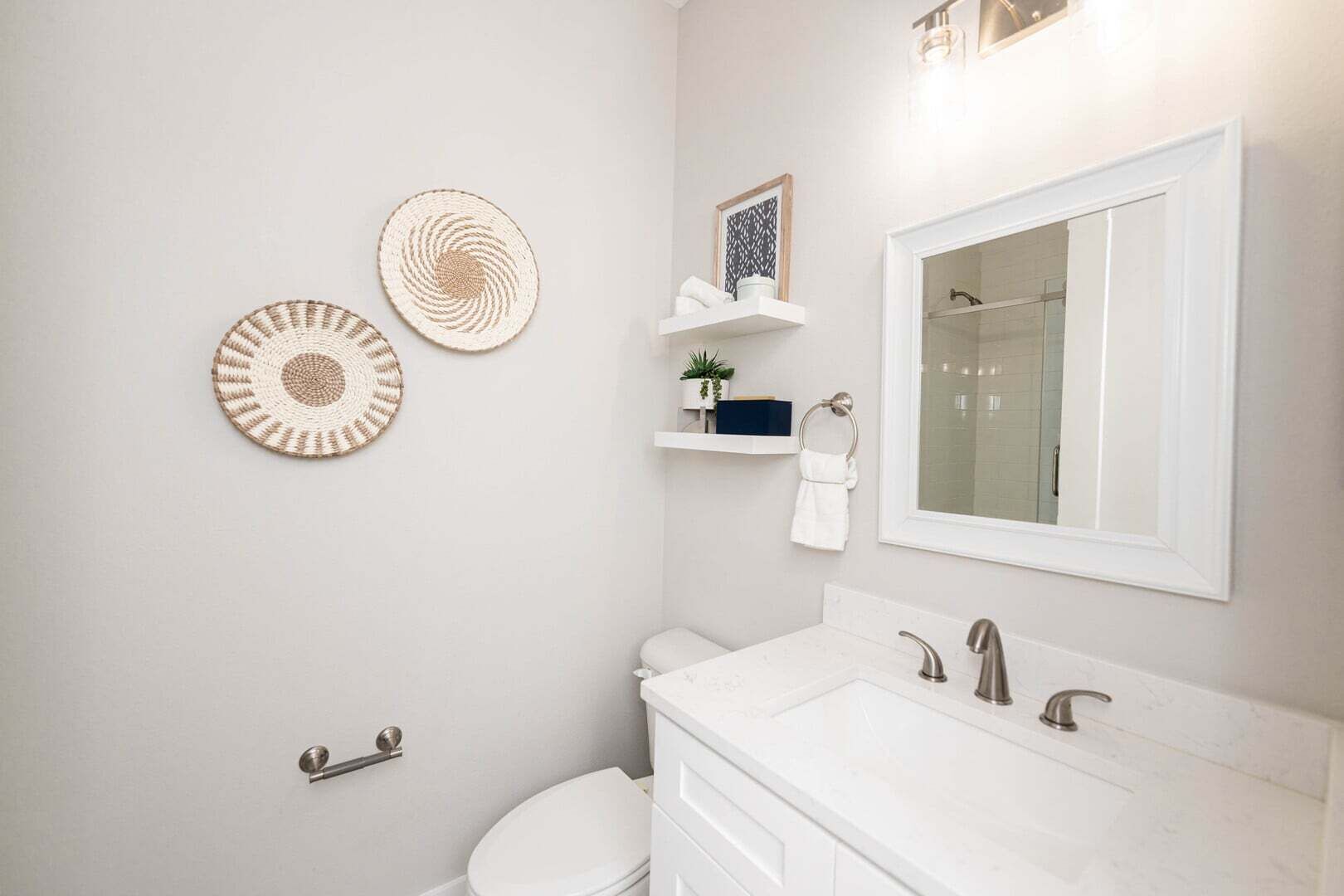 A bathroom with a toilet, sink, and mirror. There are two wall-mounted circular rugs and a shelf with a towel and a small plant.
