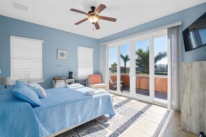 Un dormitorio con cama, escritorio, silla, ventilador de techo y vistas al exterior.