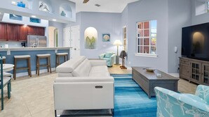 Ein modernes Wohnzimmer mit einer Couch, einem Fernseher und einer Küchenzeile mit Barhocker.