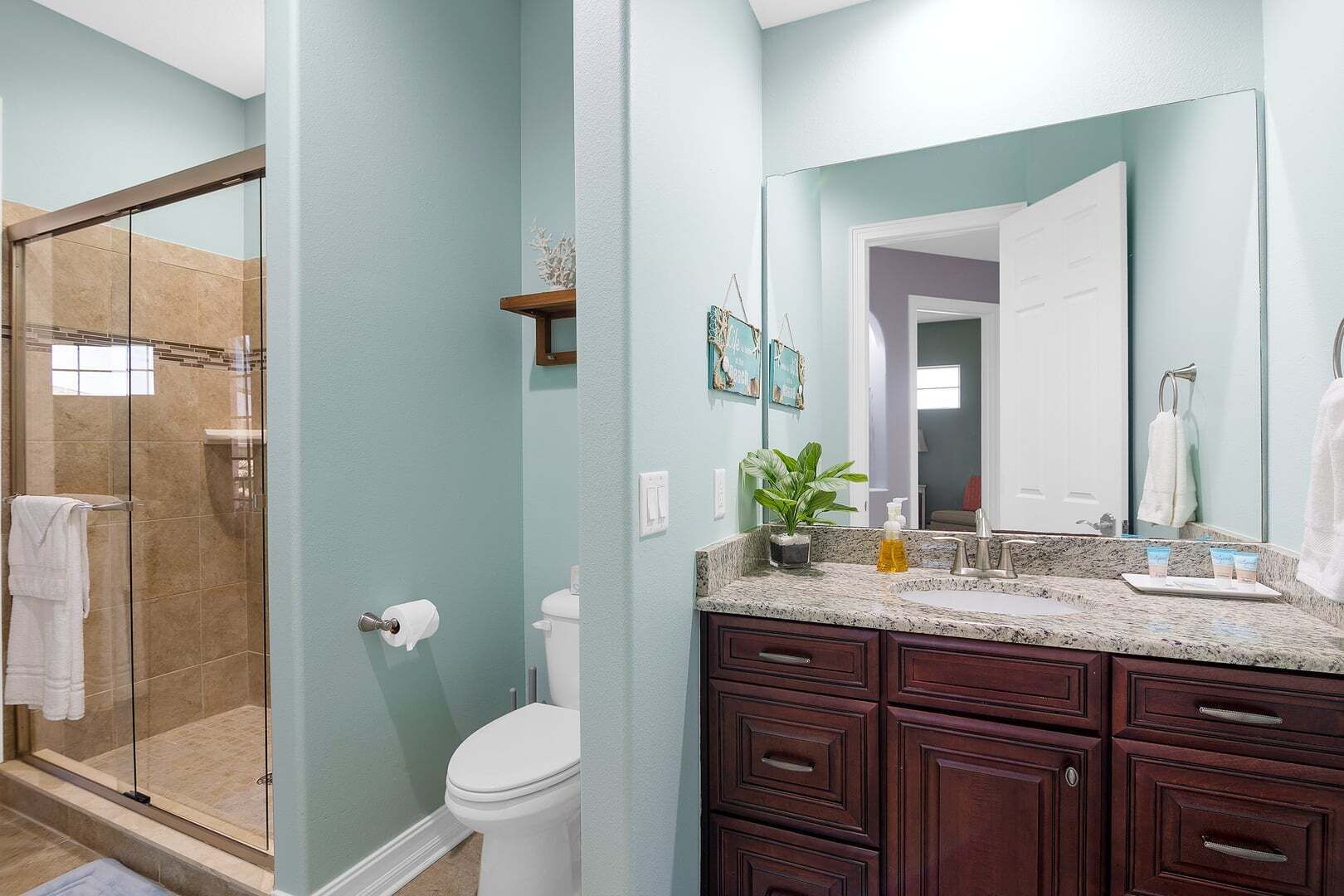 A bathroom with a glass shower enclosure, a toilet, a sink with a mirror, and dark wooden cabinets.