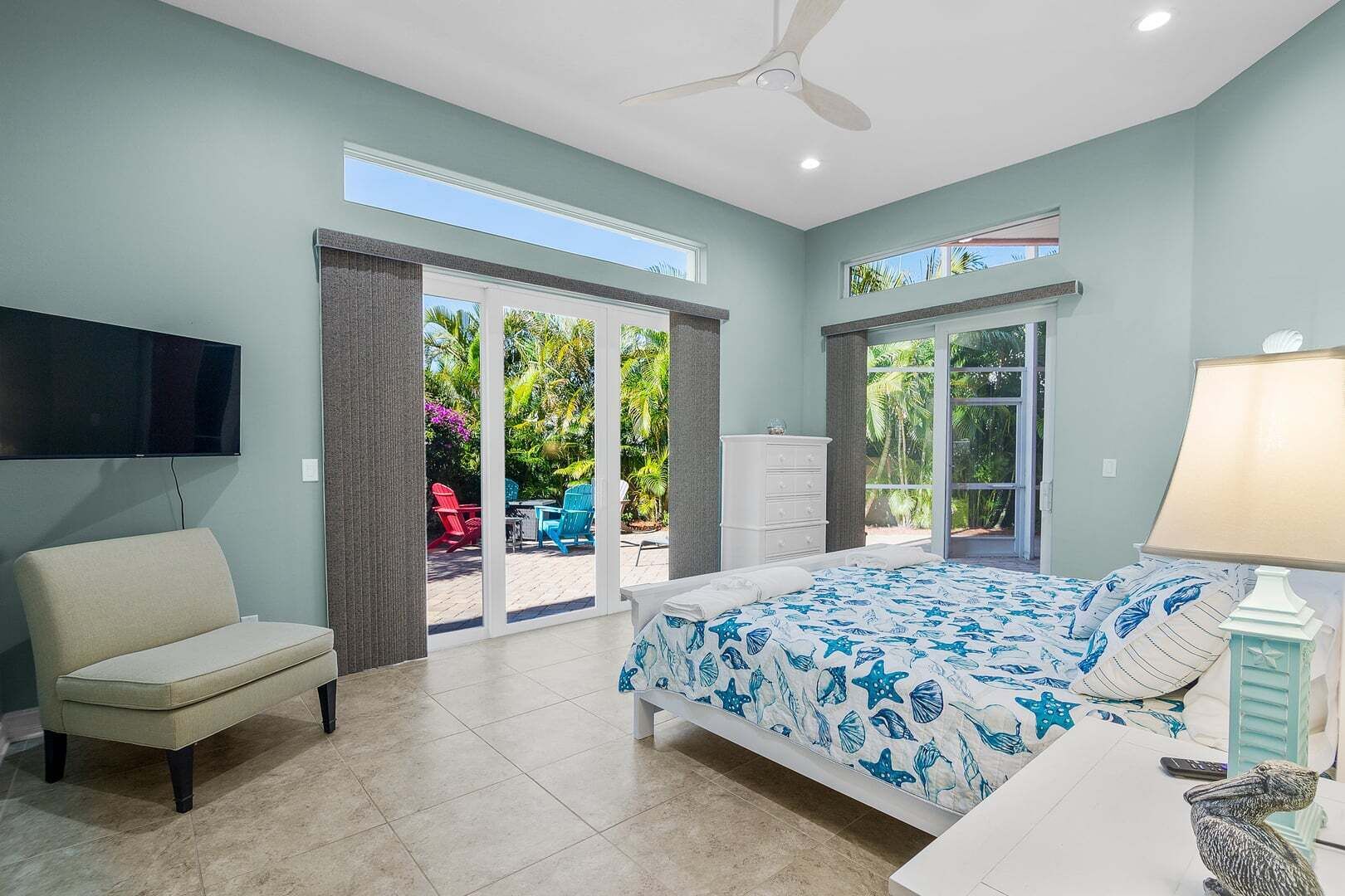A bedroom with a bed, a TV, a chair, a dresser, and a view of the outdoors.