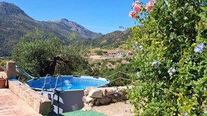 Una piscina con vistas a montañas, rodeada de vegetación y un muro de piedra.