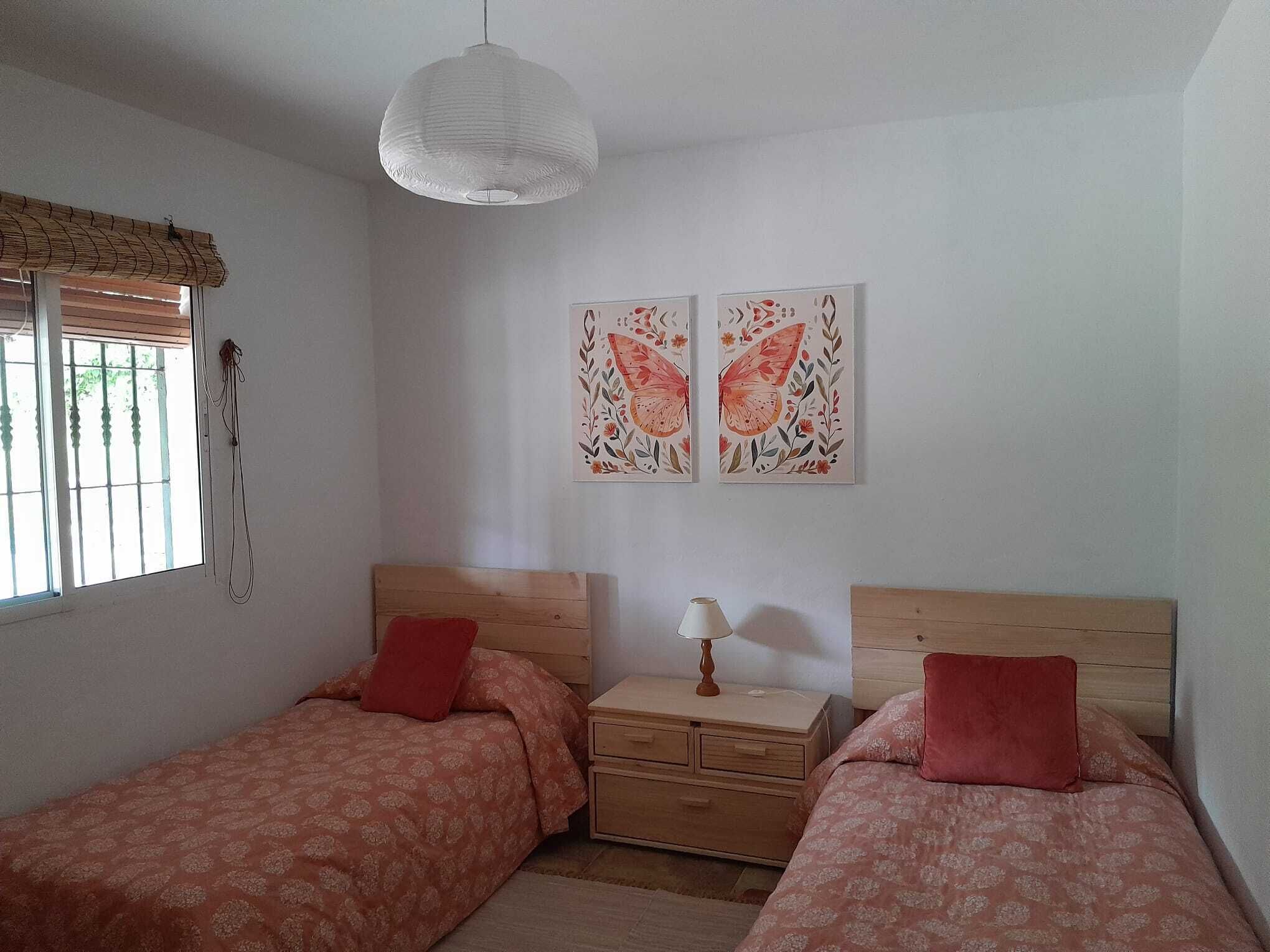 Une chambre avec deux lits simples, une table de chevet, une lampe et deux tableaux accrochés au mur.