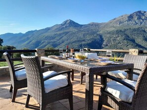 A wicker table set outdoors with a mountain view, a bottle of wine, and a bowl of salad. - El Higuerón. Beautiful retreat with a wonderful mountain view (Jimera de Líbar)