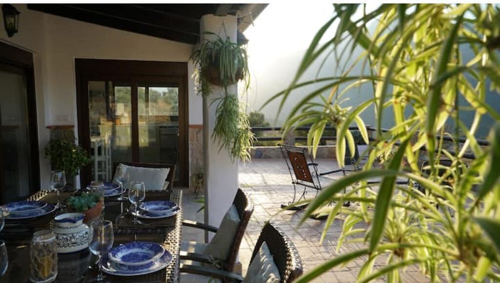 Een terras met eettafels voor twee personen, stoelen en hangplanten.