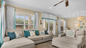 A spacious living room with a beige sofa set, a wooden coffee table, and a ceiling fan. - Pool Views, Minutes to Beach, Ground Floor Unit + Free Attraction Tickets! (Santa Rosa Beach)
