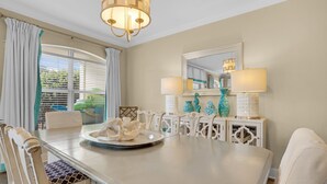 A dining room with a round table, white chairs, a chandelier, and a window with curtains. - Pool Views, Minutes to Beach, Ground Floor Unit + Free Attraction Tickets! (Santa Rosa Beach)
