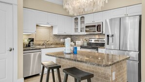 A modern kitchen with white cabinetry, granite countertops, stainless steel appliances, and a central island with stools. - Pool Views, Minutes to Beach, Ground Floor Unit + Free Attraction Tickets! (Santa Rosa Beach)