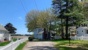 A residential street with houses, a white picket fence, and a clear sky.