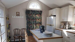 A kitchen with a central island, white cabinets, a window with a curtain, and a dining area with two chairs.
