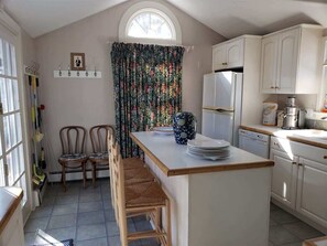 A kitchen with a central island, white cabinets, a window with a curtain, and a dining area with two chairs.
