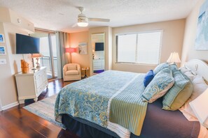 Un dormitorio con cama, ventilador de techo, televisor, cómoda, silla y ventana con persianas.