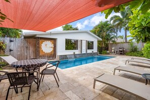 A backyard with a swimming pool, a covered patio, and a house with a white exterior.