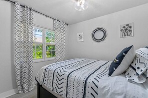 A bedroom with a bed, patterned curtains, a window, and wall art.