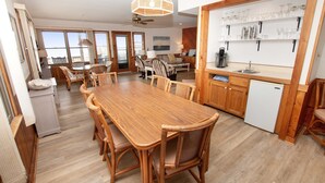 A spacious kitchen with a wooden dining table and chairs, a refrigerator, and a built-in shelf with glassware.