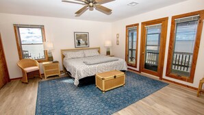 A bedroom with a bed, a ceiling fan, a window with a view, a nightstand, a chair, and a wooden chest.
