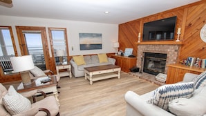 A spacious living room with a fireplace, wooden walls, and a large TV mounted above it.