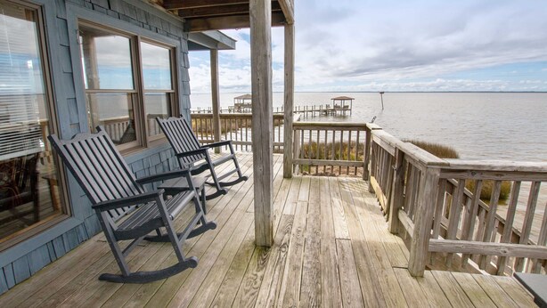 A wooden deck with rocking chairs overlooking a body of water.