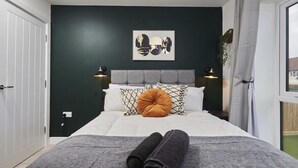 Un lit bien fait, avec une couverture grise, un oreiller marron et deux serviettes enroulées.