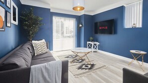 Un salon moderne avec un mur d’accent bleu, un canapé gris, une table basse blanche et un téléviseur fixé au mur.