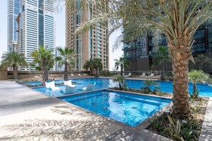A swimming pool area with palm trees and modern buildings in the background.
